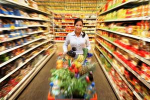 Une femme pousse son caddie rempli de produits dans un rayon de supermarché
